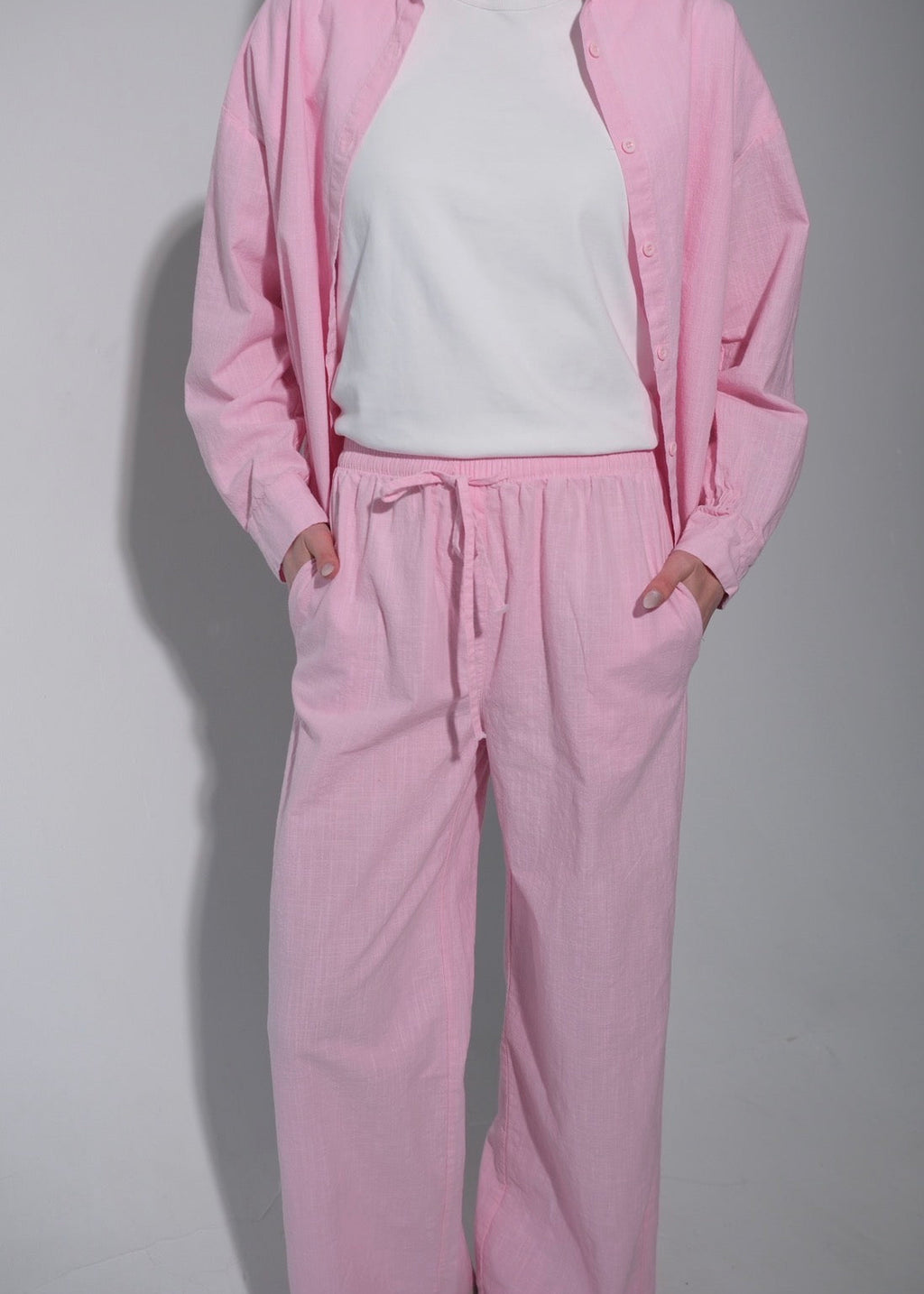Person wearing a pink tracksuit with a white shirt on a plain background