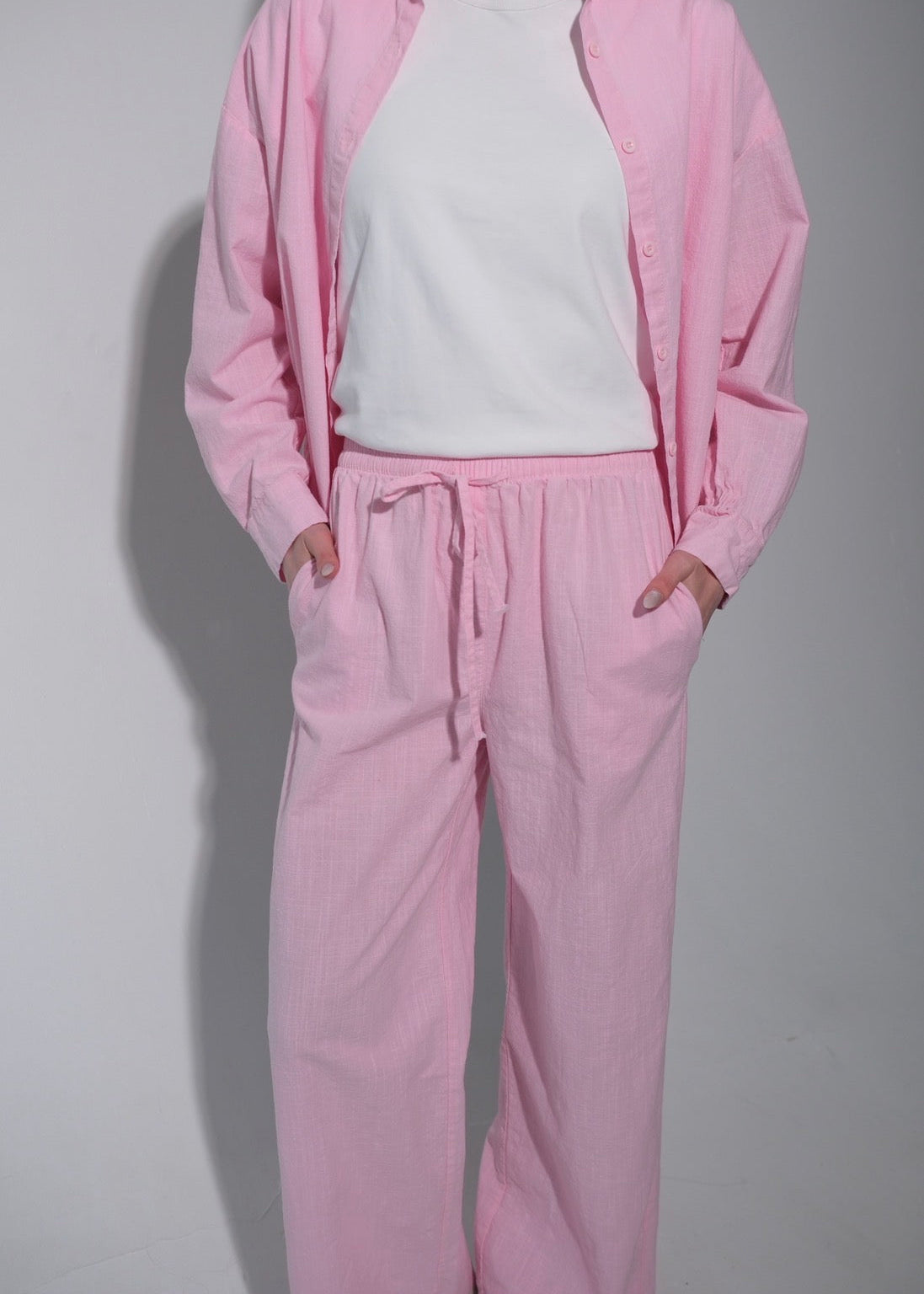Person wearing a pink tracksuit with a white shirt on a plain background