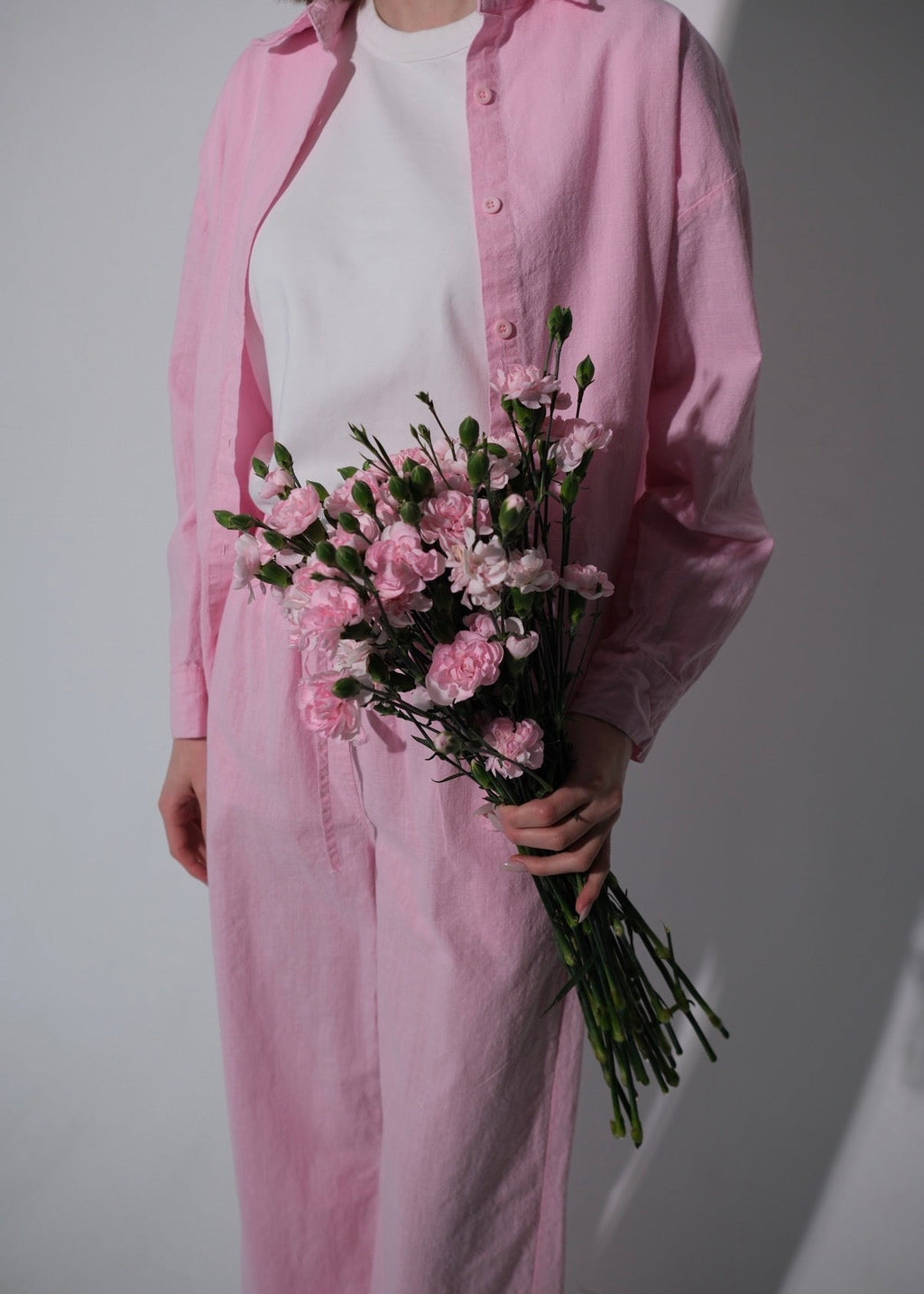 Person wearing a pink shirt and holding a bouquet of pink flowers against a plain background