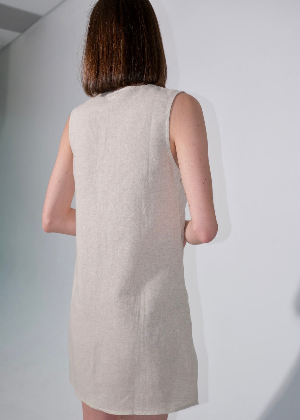 Woman wearing a beige sleeveless dress against a white background
