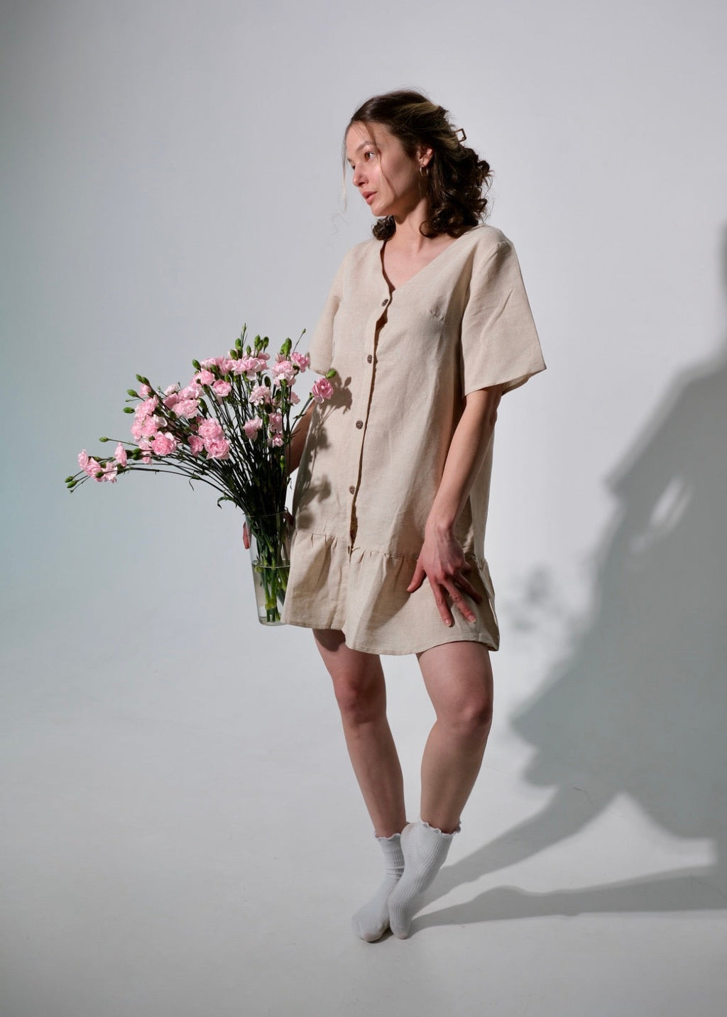 Woman in a beige dress holding flowers against a plain background