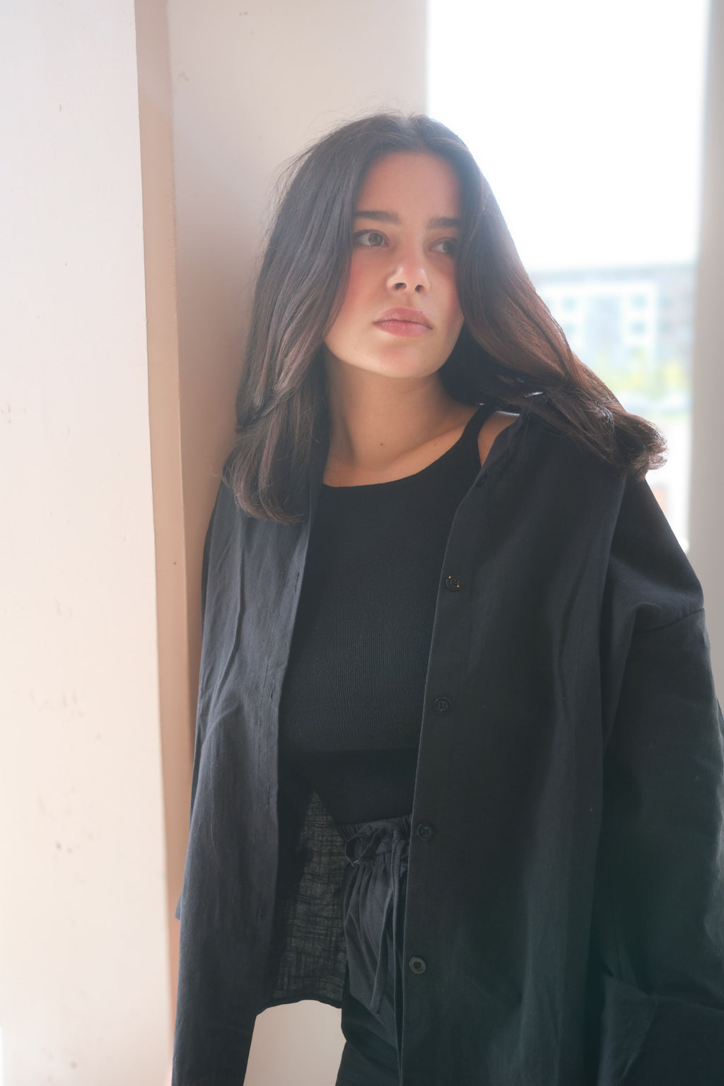 Woman wearing a dark green coat leaning against a wall indoors.
