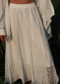 A white bohemian-style maxi skirt with vertical pleats and lace trim, worn by a model outdoors.