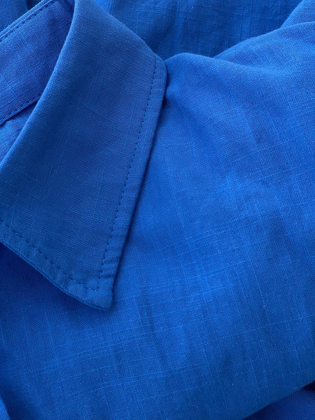 A close-up of a bright blue textured fabric with a pointed collar and visible stitching.