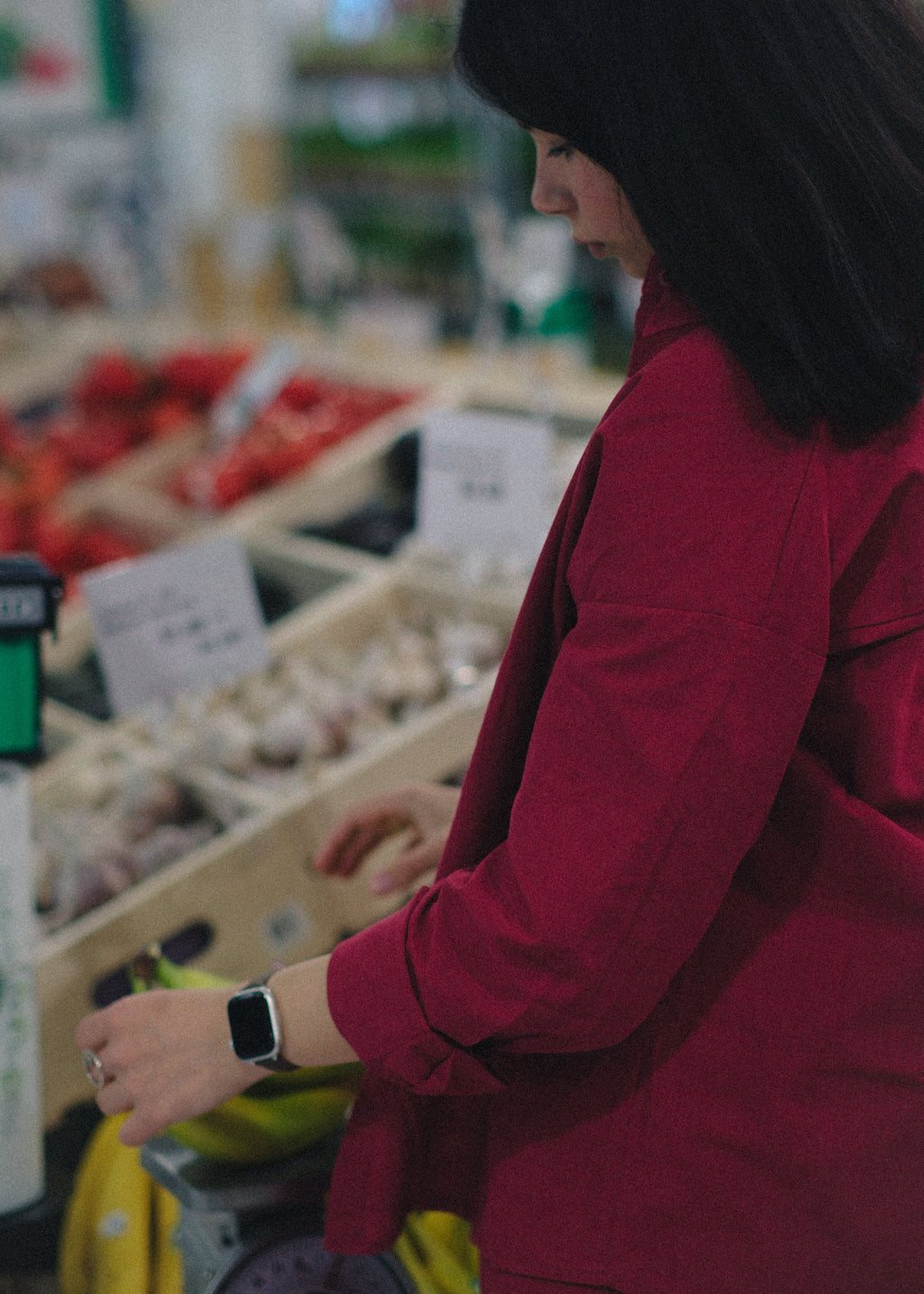 Person in a red coat standing in a grocery store produce section