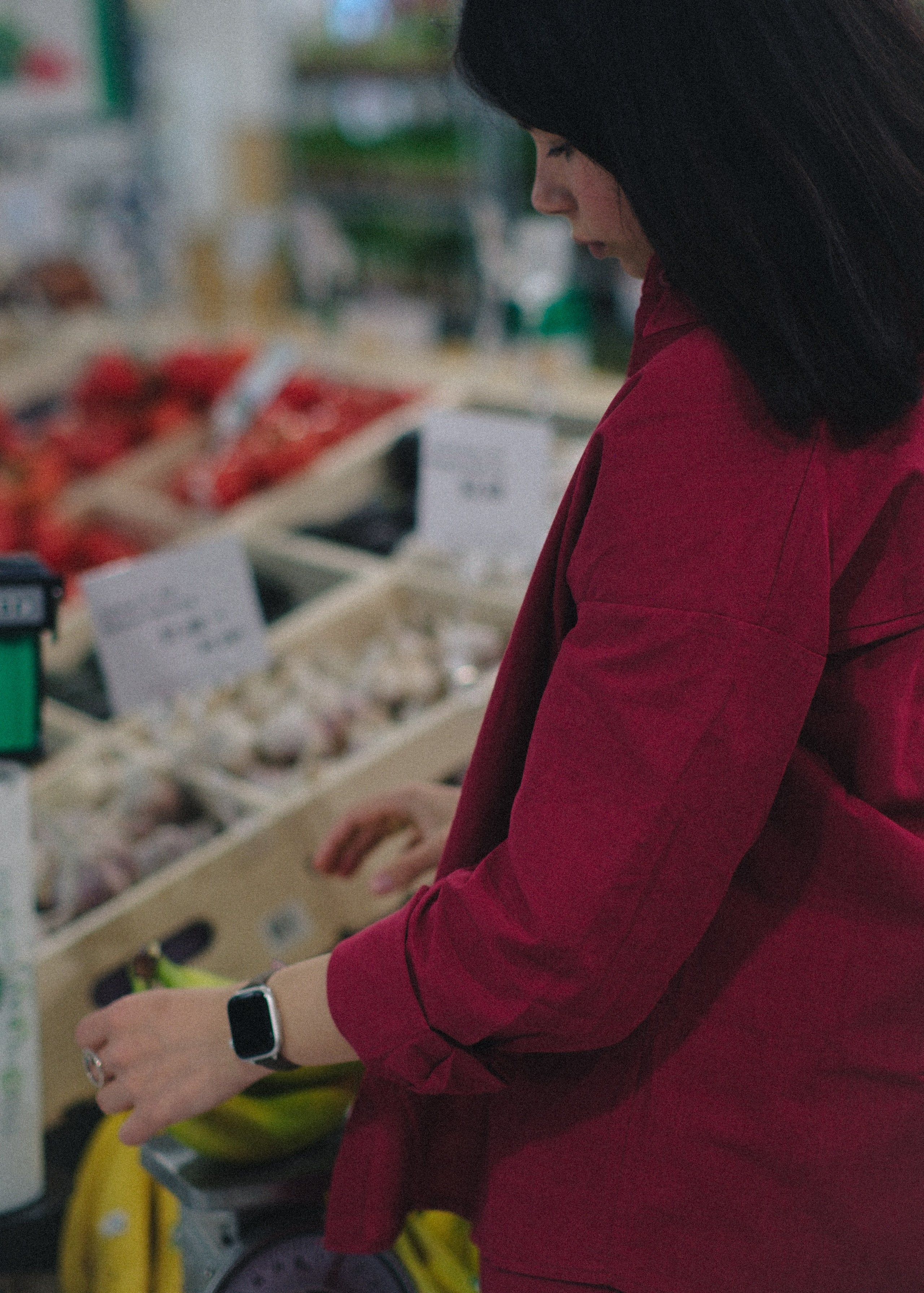 Person in a red coat standing in a grocery store produce section