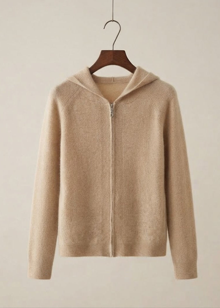 A beige knit zip-up hoodie sweater hanging on a wooden hanger against a solid light beige background.
