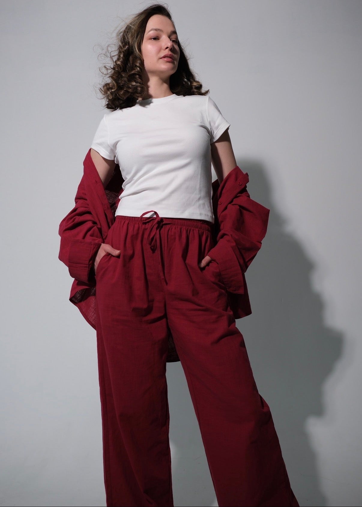 Woman wearing a white shirt and red pants against a gray background