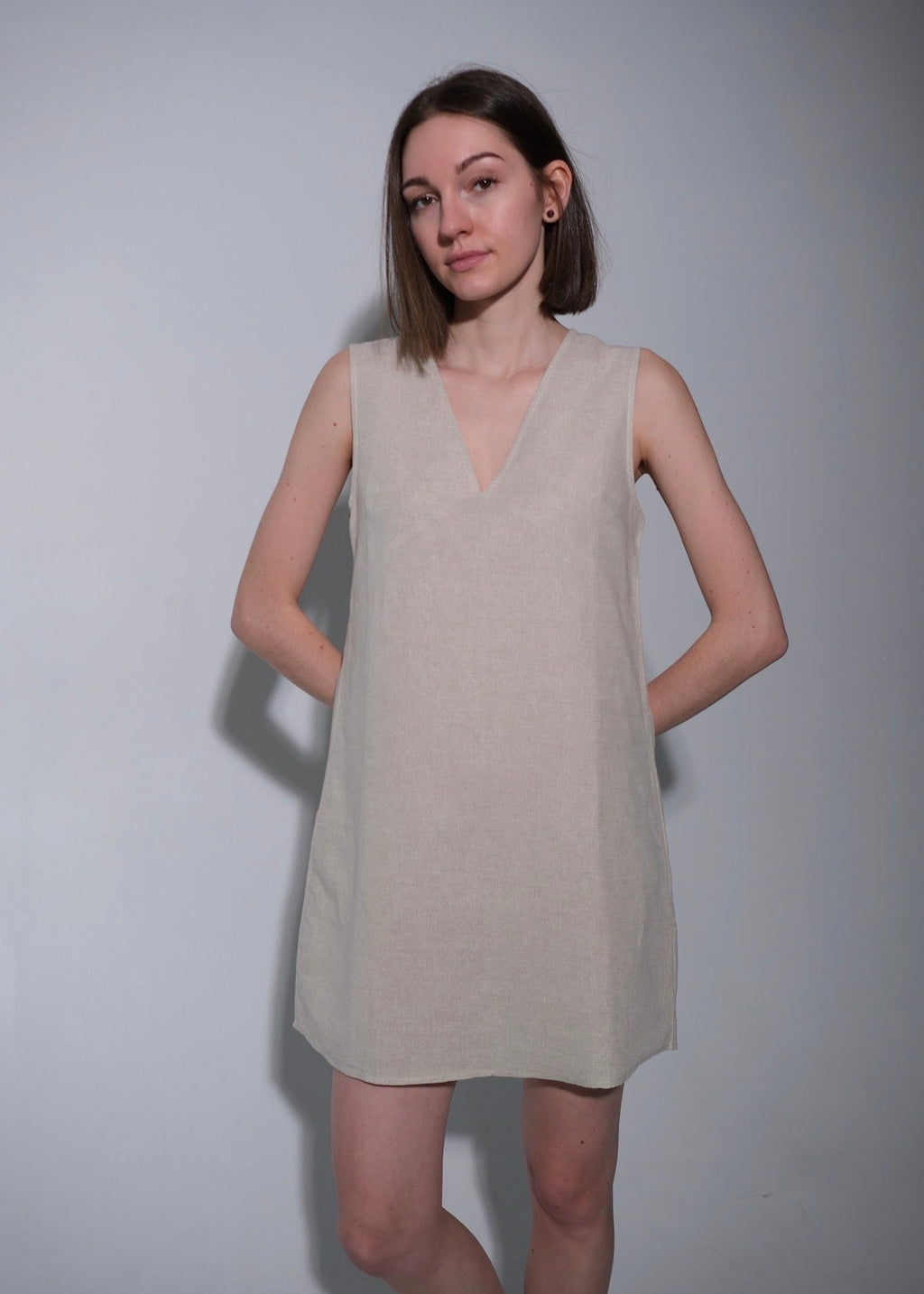Woman wearing a beige sleeveless dress against a plain background