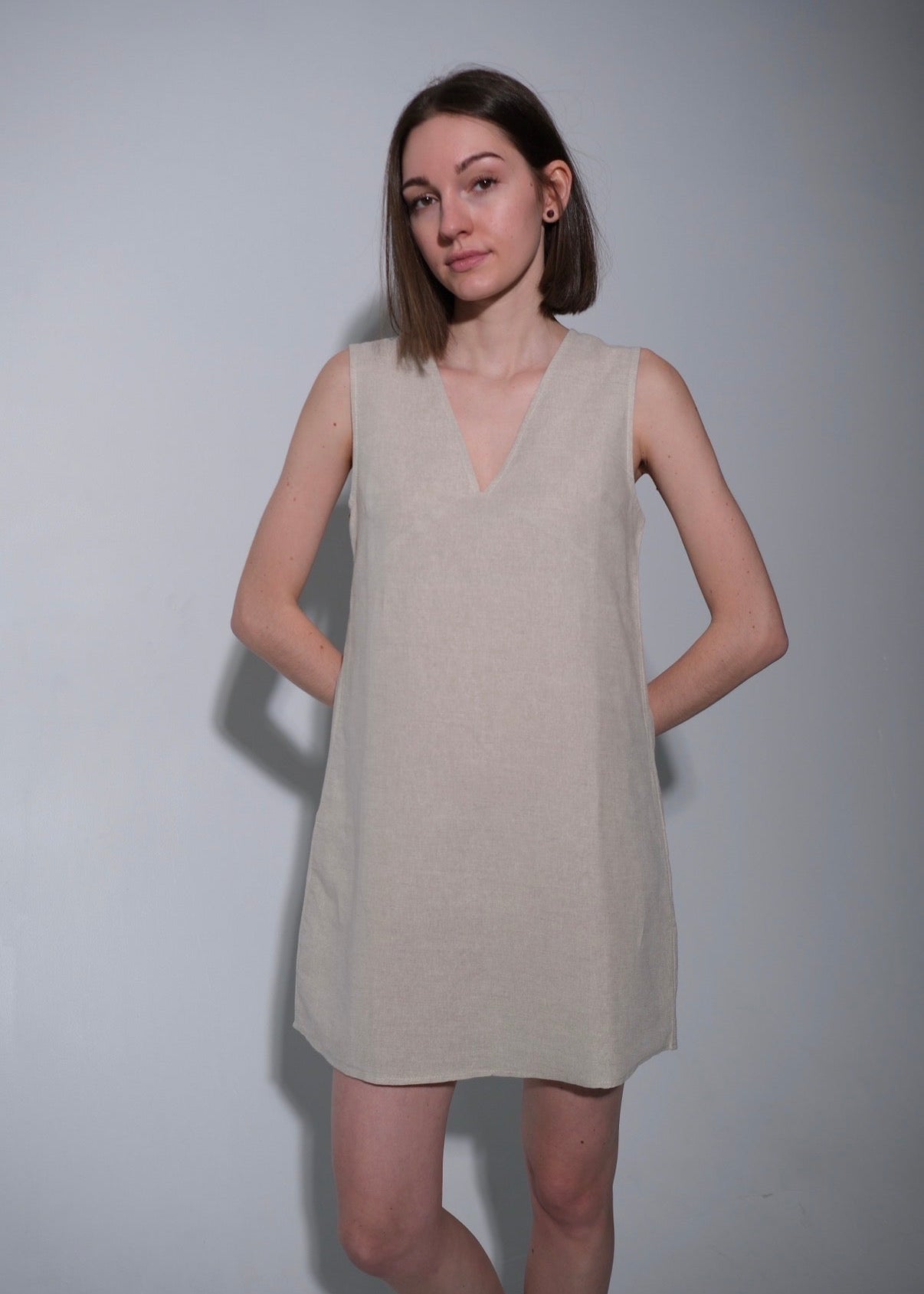 Woman wearing a beige sleeveless dress against a plain background