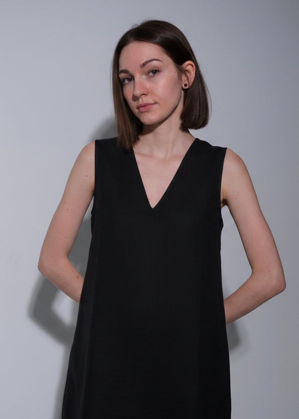 Woman wearing a beige sleeveless dress against a plain background