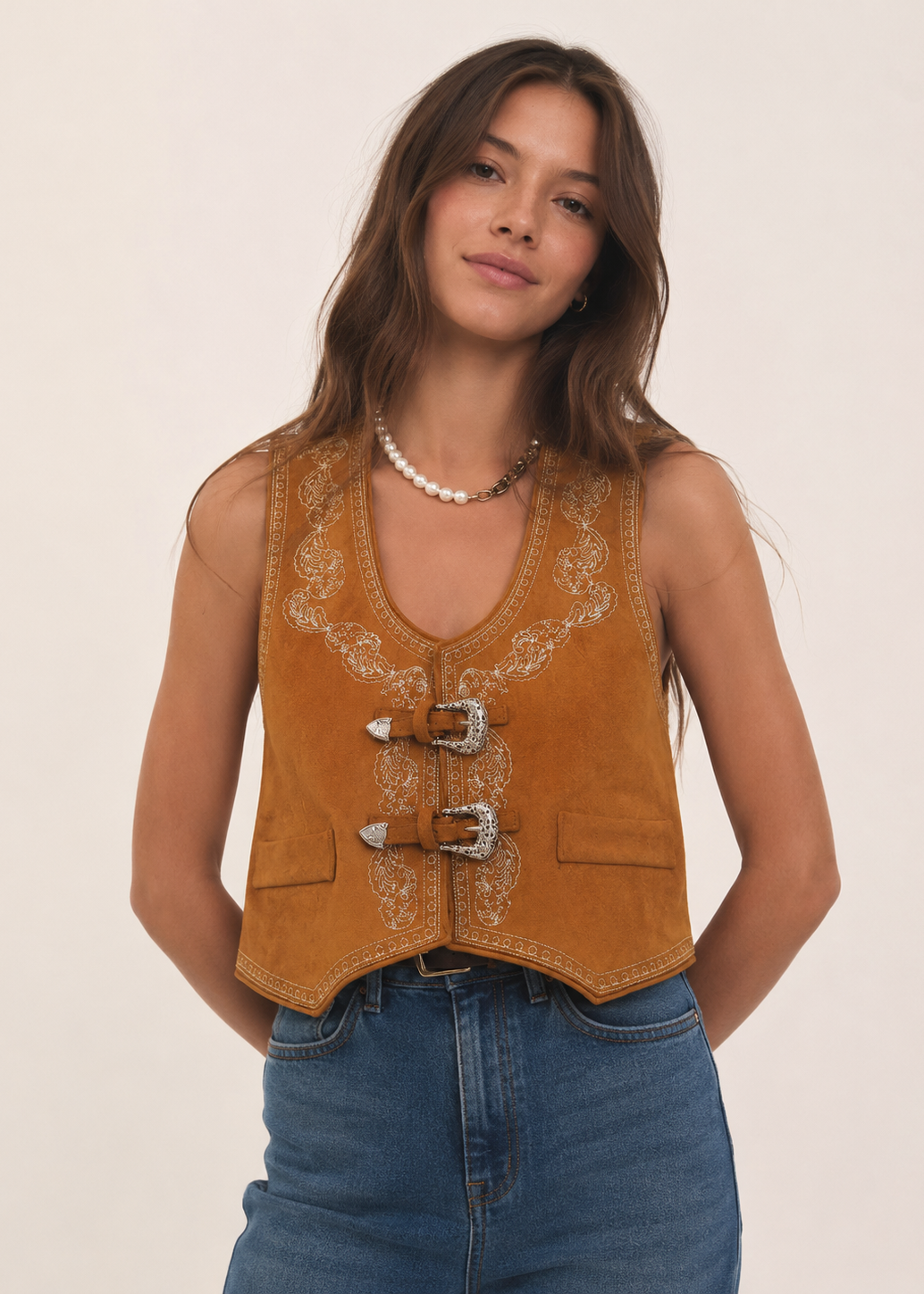 Woman wearing a brown embroidered vest and blue jeans on a beige background