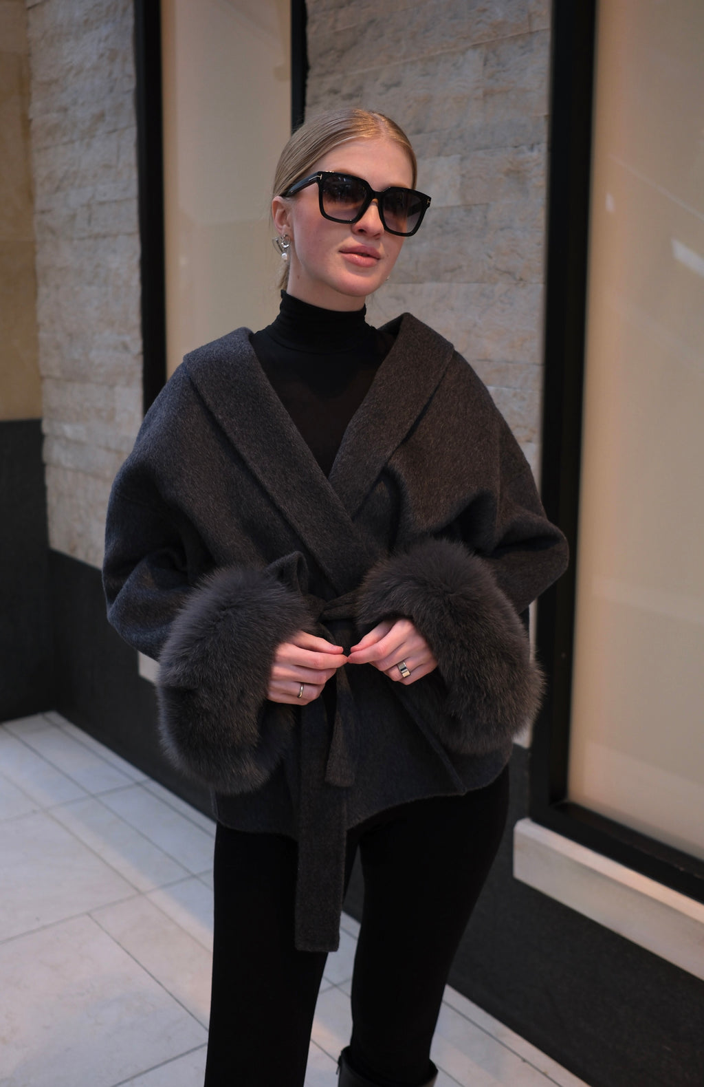 Woman wearing a charcoal grey luxury wool wrap coat with genuine rabbit fur cuffs, belted waist, oversized collar and elegant winter style.