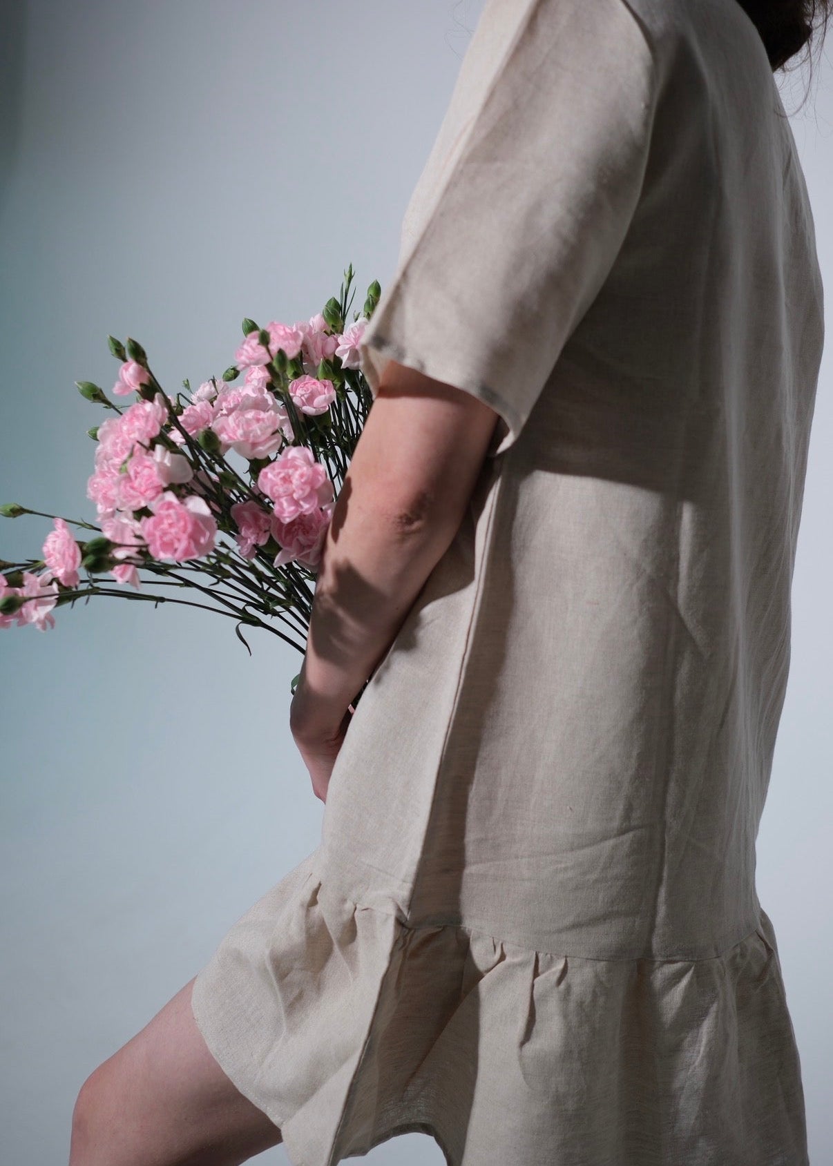 Person wearing a beige dress holding pink flowers against a light gray background