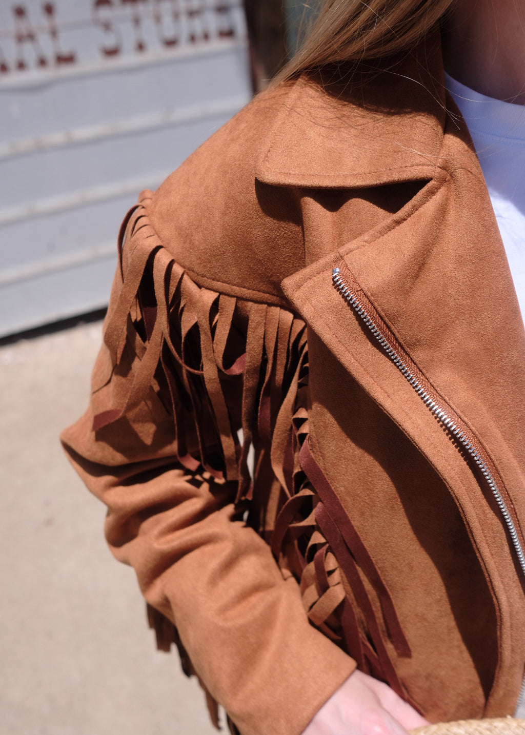 Brown suede handbag with fringe details held by a person.