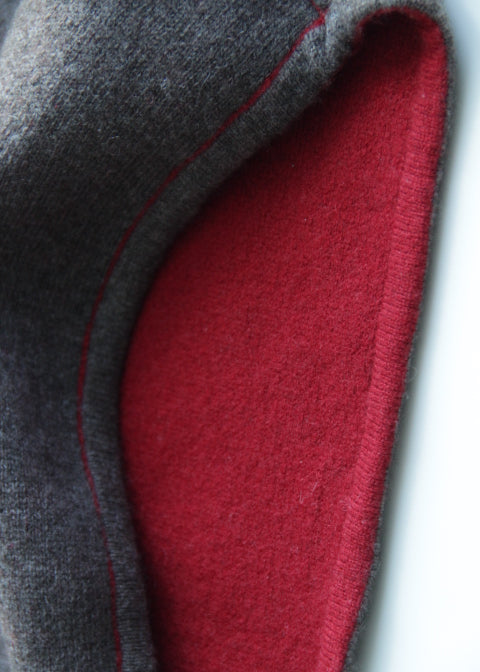 Close-up of a folded fabric item showing a dark gray outer layer and a red inner layer with a thin red stitched edge.