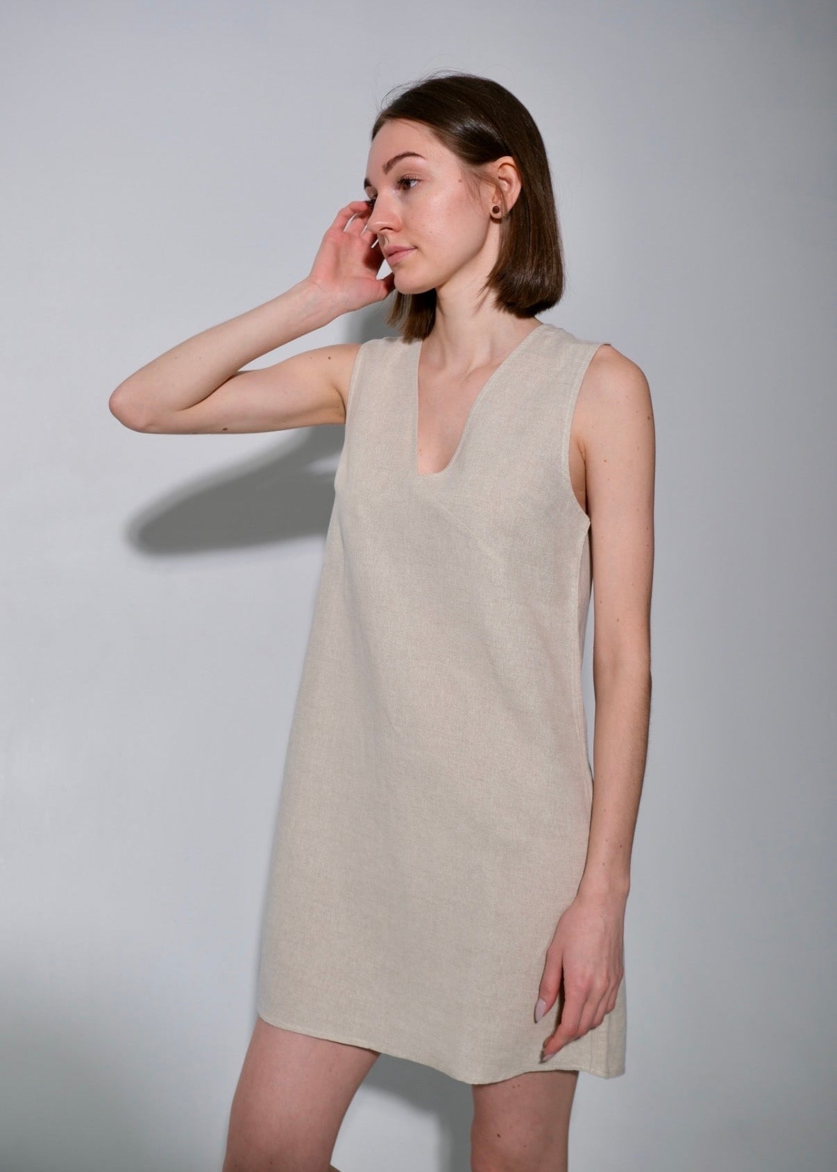 Woman wearing a beige sleeveless dress against a plain background