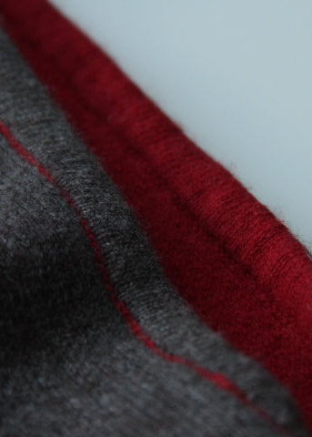 Close-up of a dark gray knit fabric with a contrasting deep red inner lining or trim, showing the texture and stitching detail.