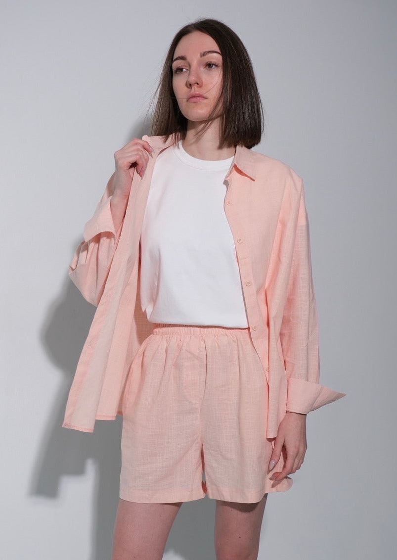 Person wearing a light pink outfit with a jacket and shorts on a plain background