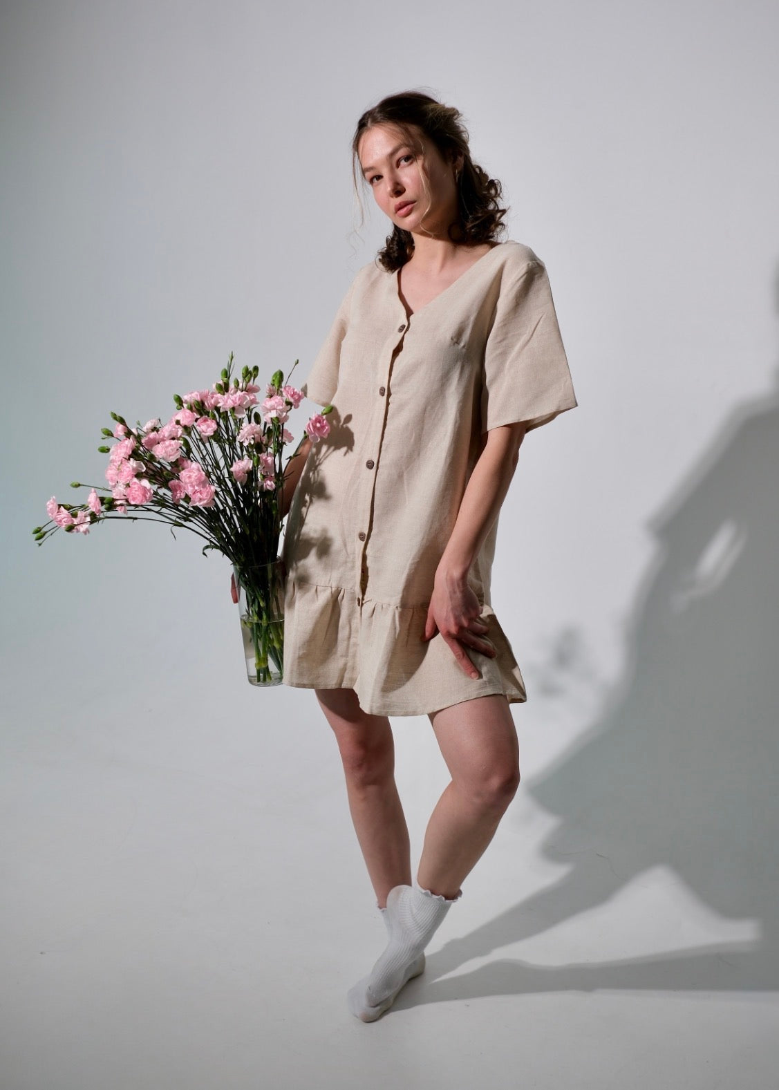 Woman in a beige dress holding pink flowers against a plain background