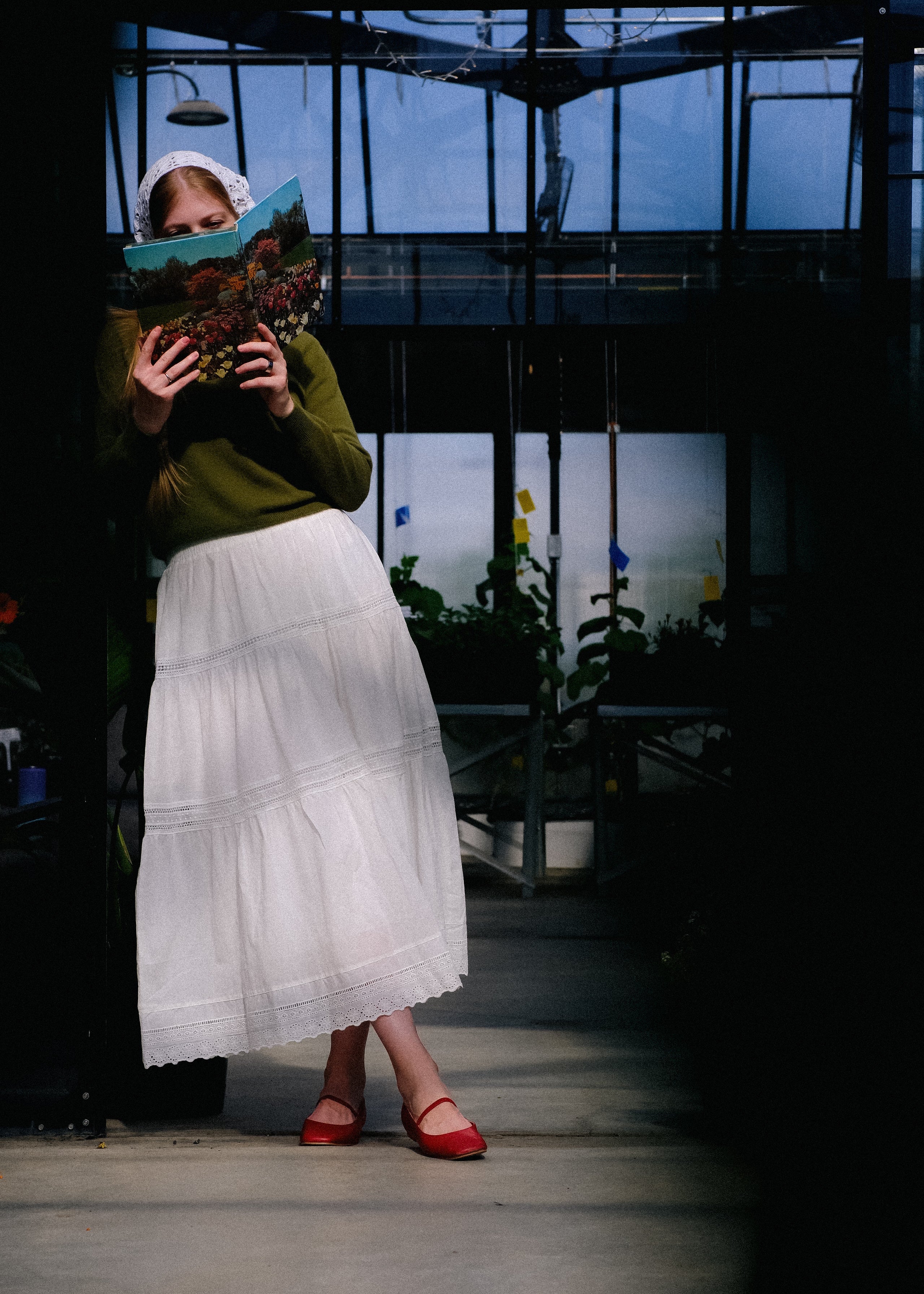 Person holding a book in a greenhouse setting