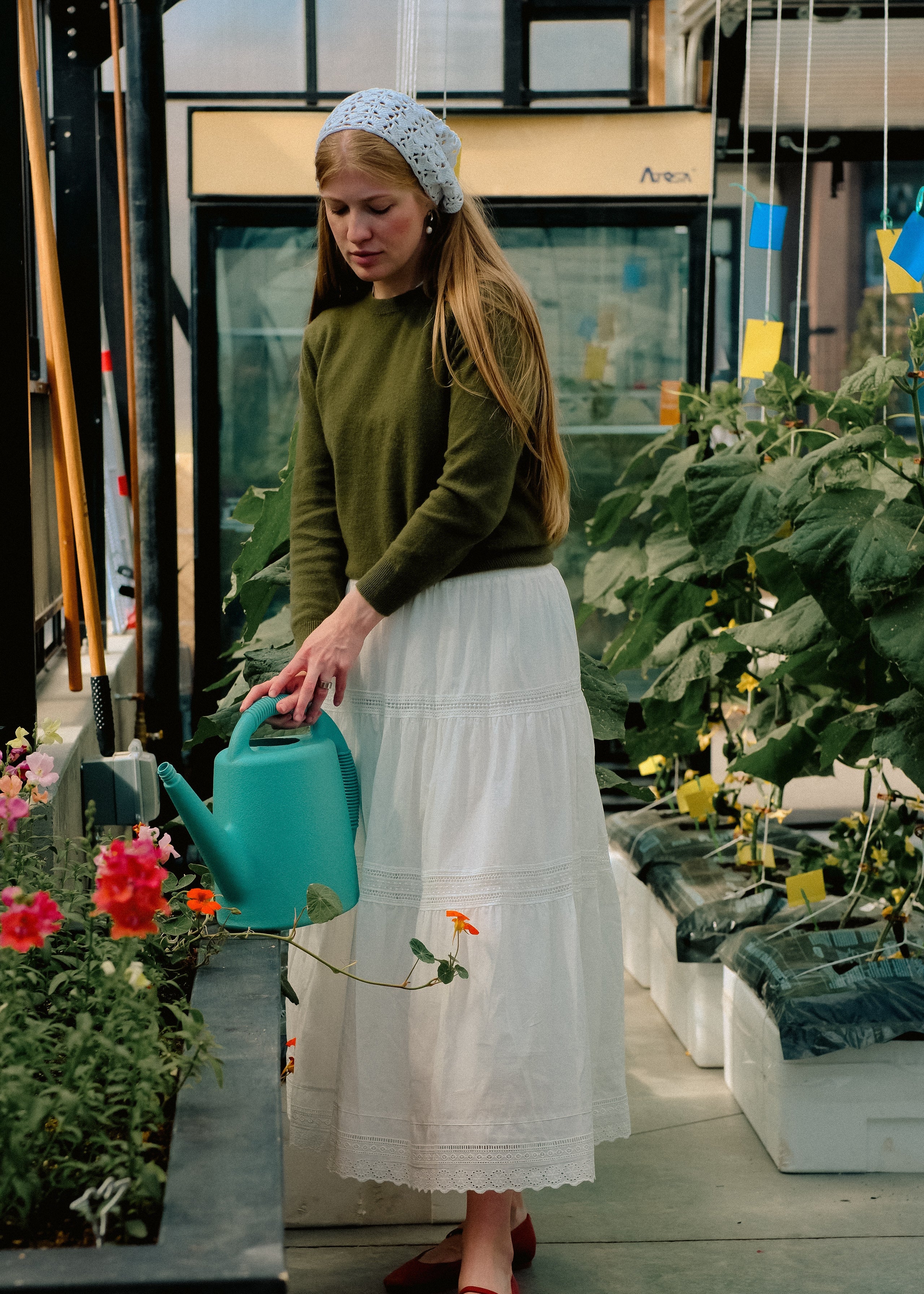 Woman holding a blue watering can in a greenhouse setting