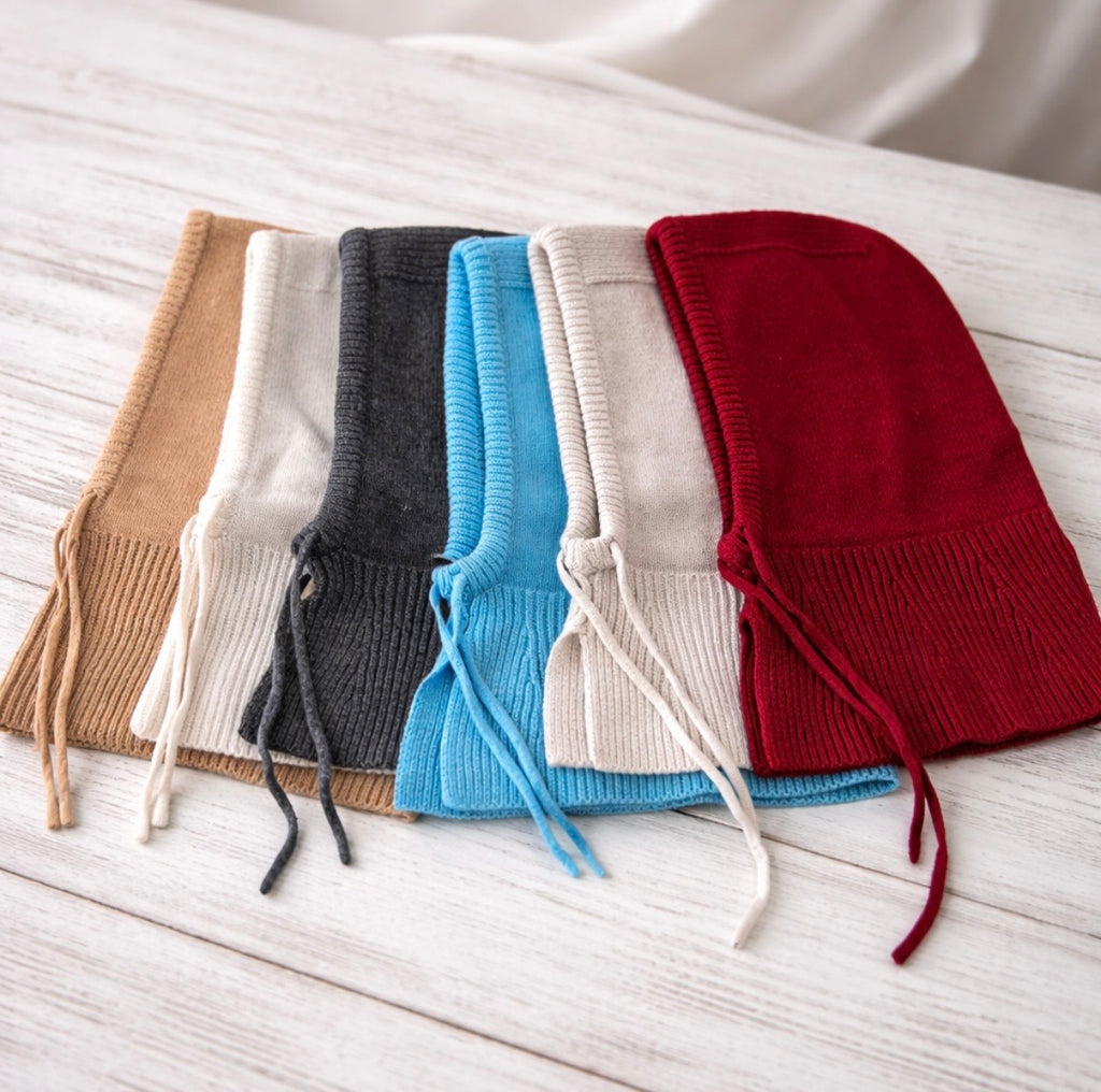 Five knit beanies in different colors arranged on a light wooden surface.