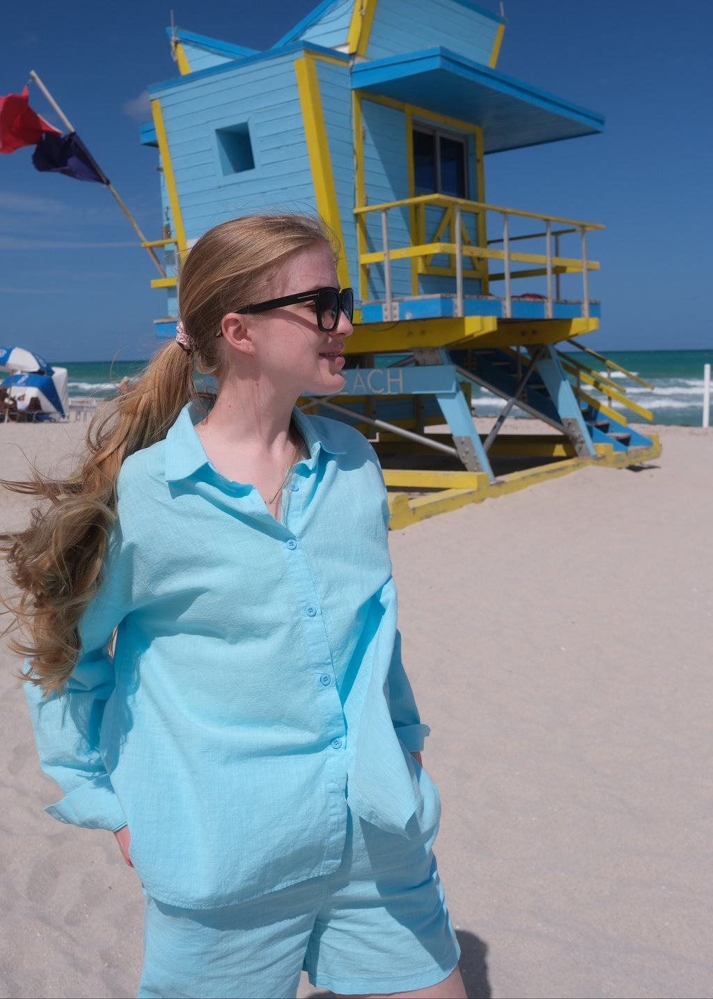 Woman in a blue shirt standing next to a small blue building with yellow accents on a clear day.