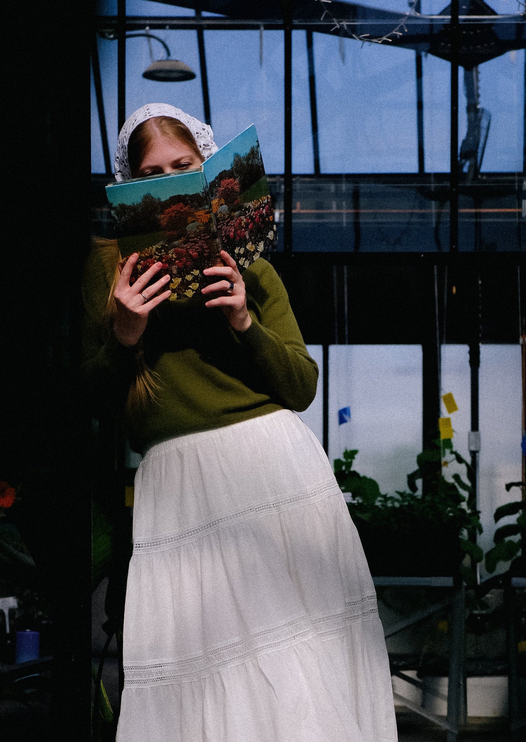 Person holding a book in a greenhouse setting