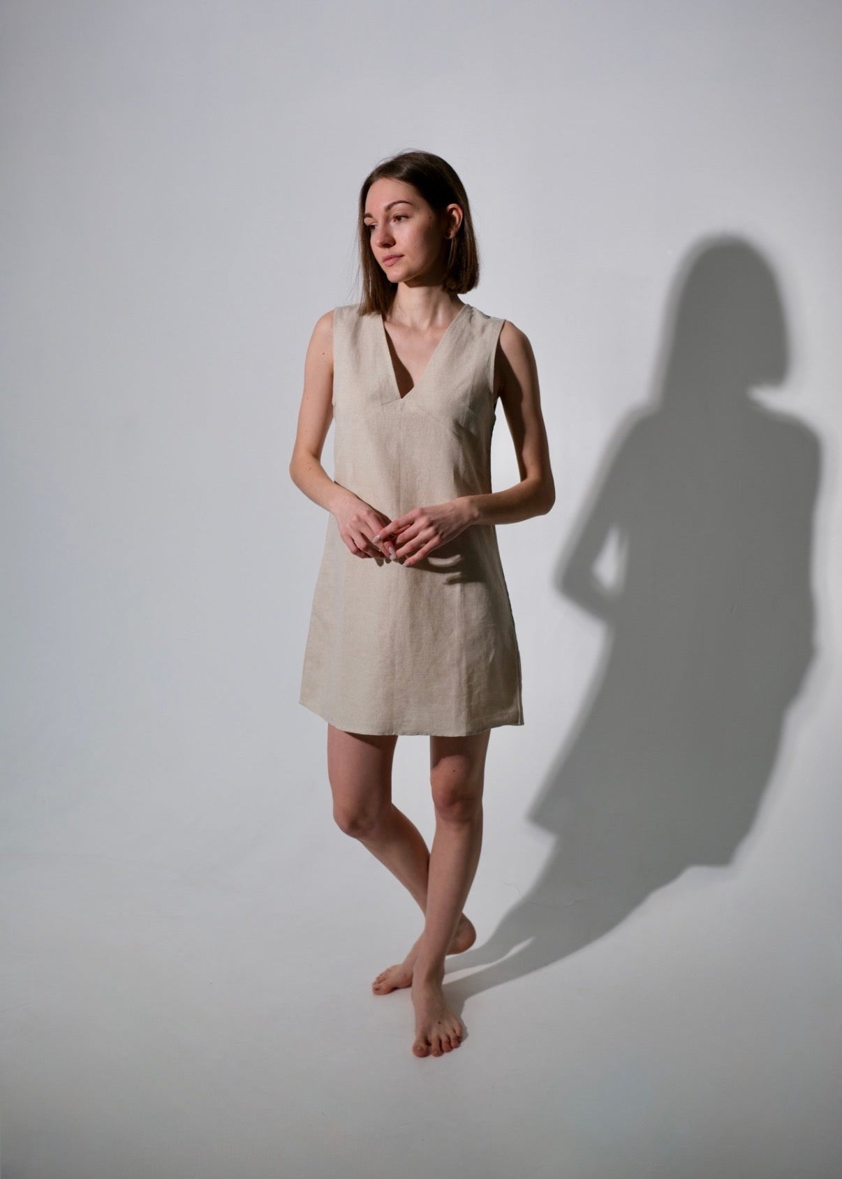 Woman wearing a beige dress standing against a white wall with a soft shadow.
