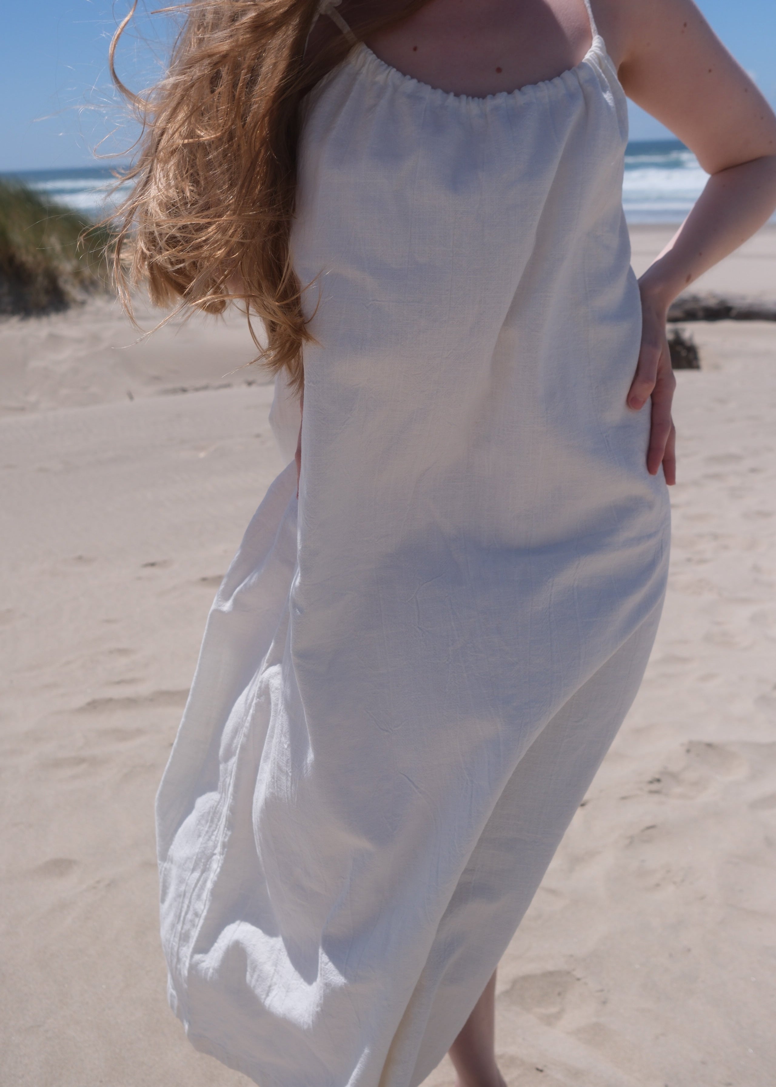 Person holding a white dress against a beach backdrop