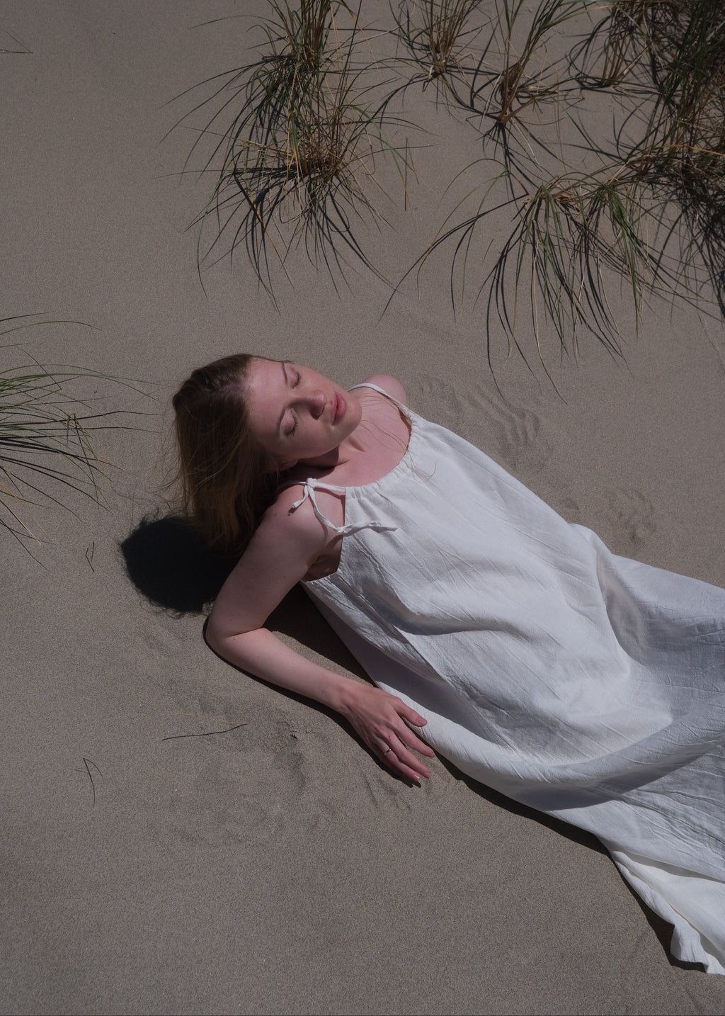 Woman in a white dress lying on sand with grasses around