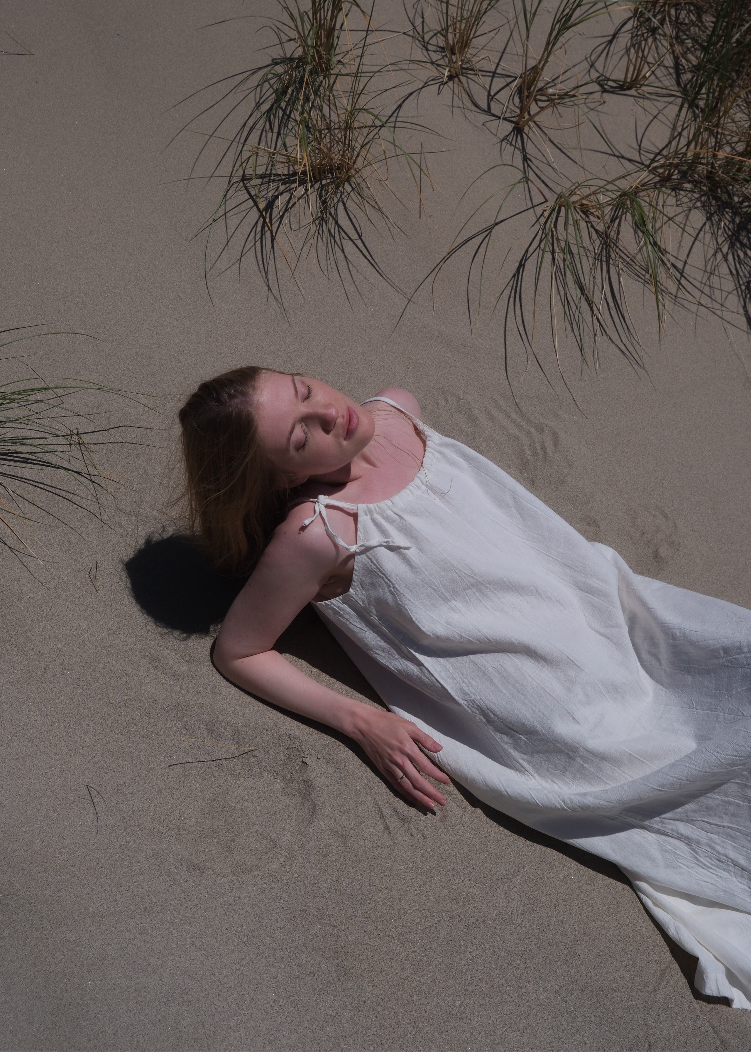 Woman in a white dress lying on sand with grasses around