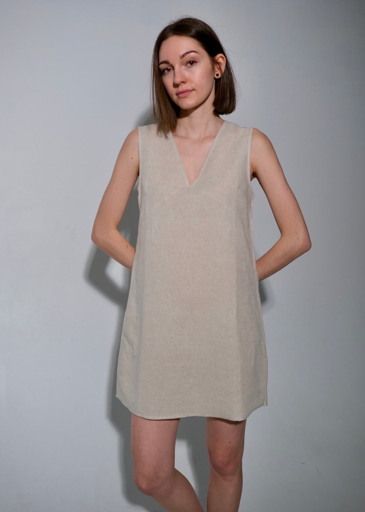 Woman wearing a beige sleeveless dress against a plain background
