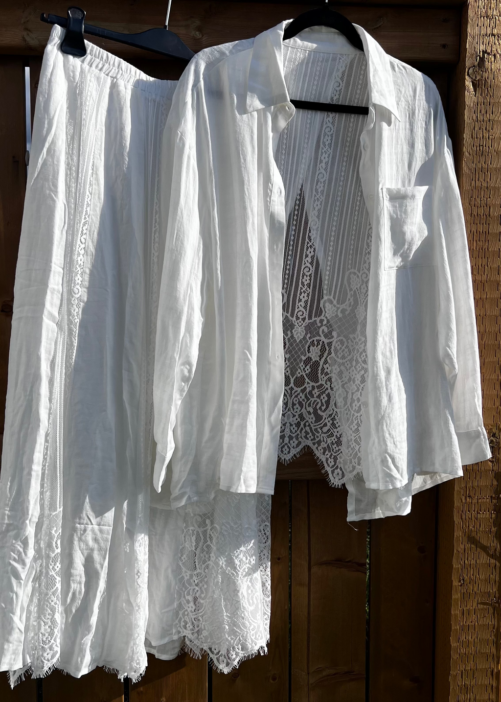 White lace shirt and pants hanging on a wooden fence with blue sky and clouds in the background.