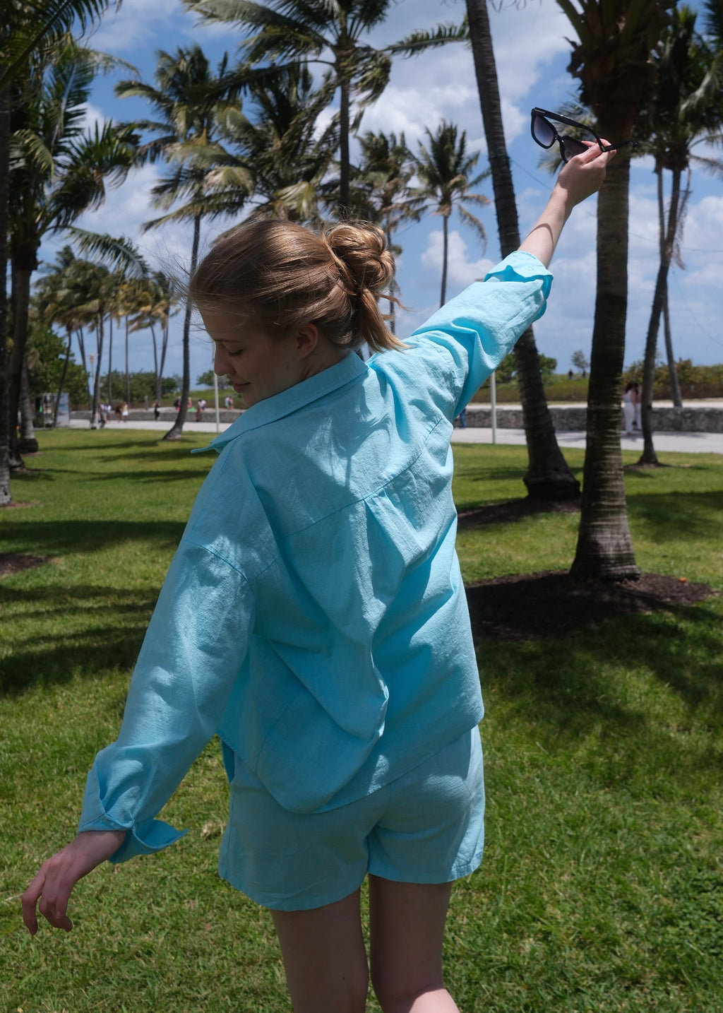 Person wearing a light blue outfit in a park with palm trees