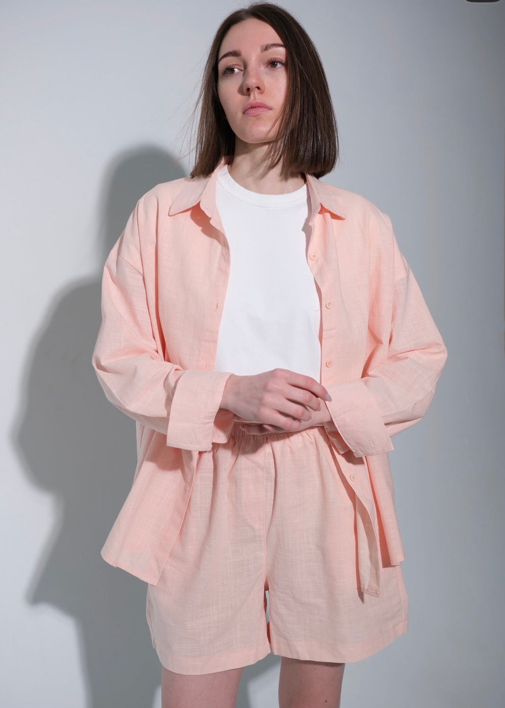 Person wearing a light pink outfit with a white shirt underneath against a plain background