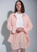 Person wearing a light pink outfit with a white shirt underneath against a plain background