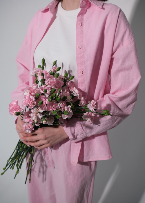 Person wearing a pink shirt and pants holding a bouquet of pink flowers against a white background