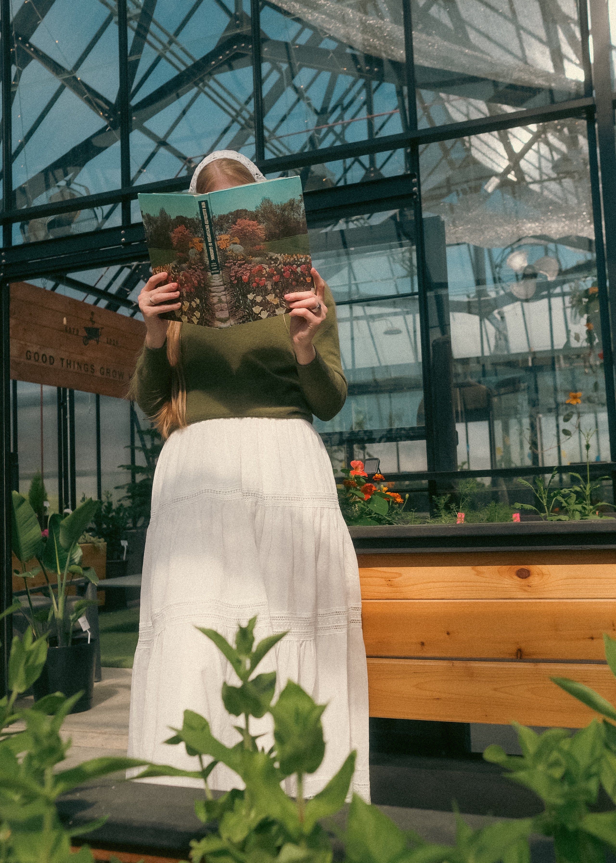 Person holding a book with plant images in a greenhouse