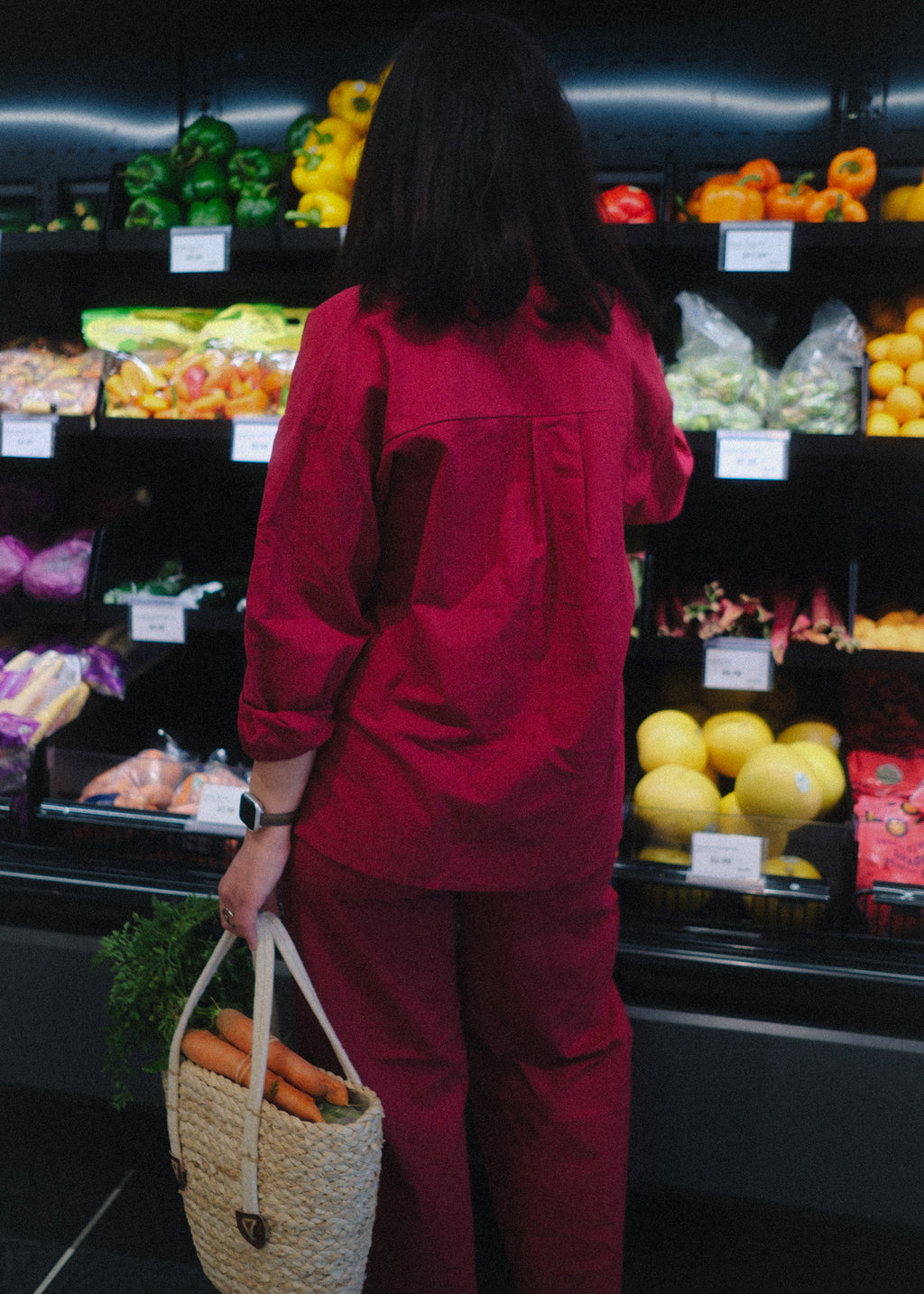 Person in a red outfit shopping in a grocery store with produce on shelves.