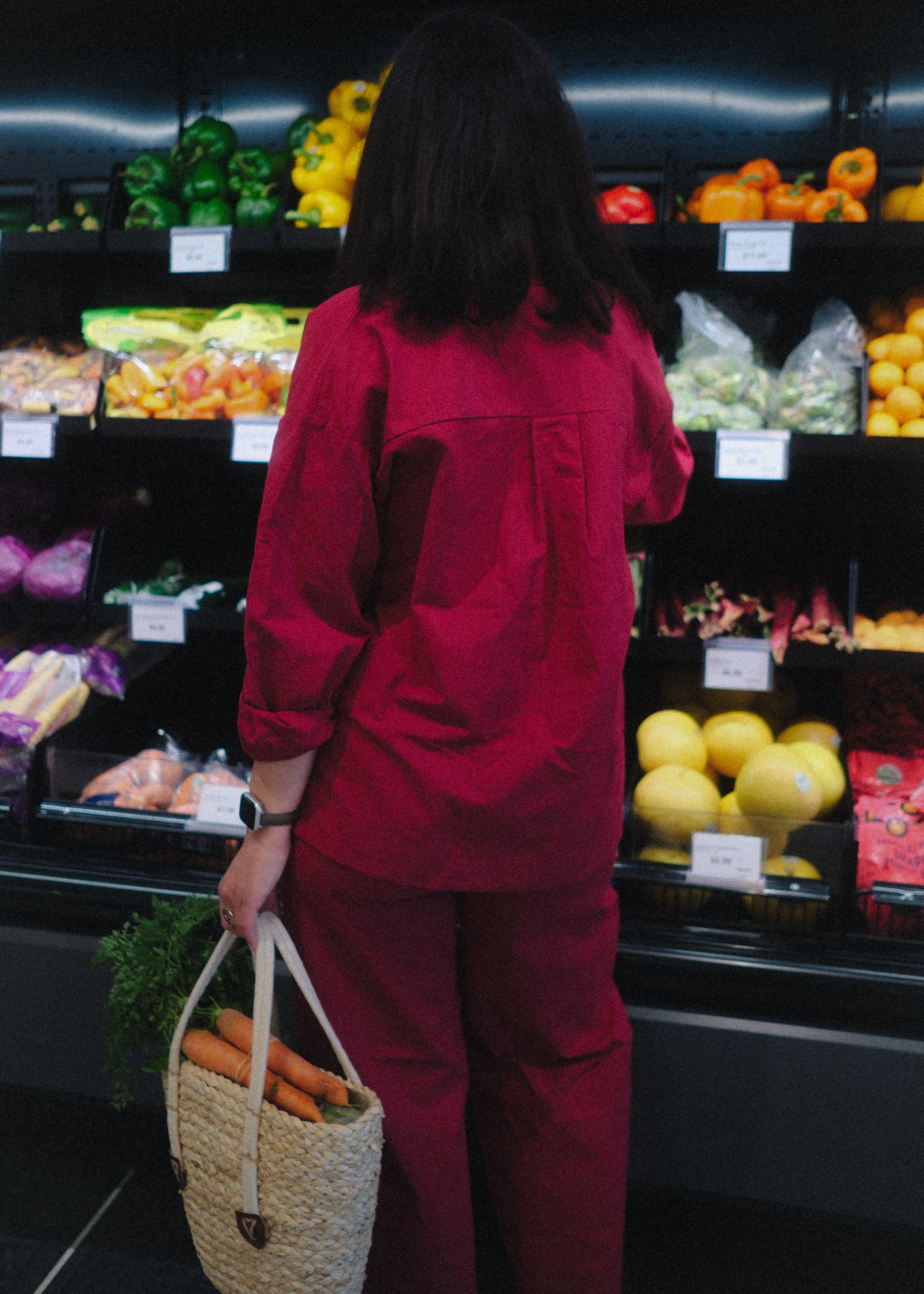 Person in a red outfit shopping in a grocery store with produce on shelves.