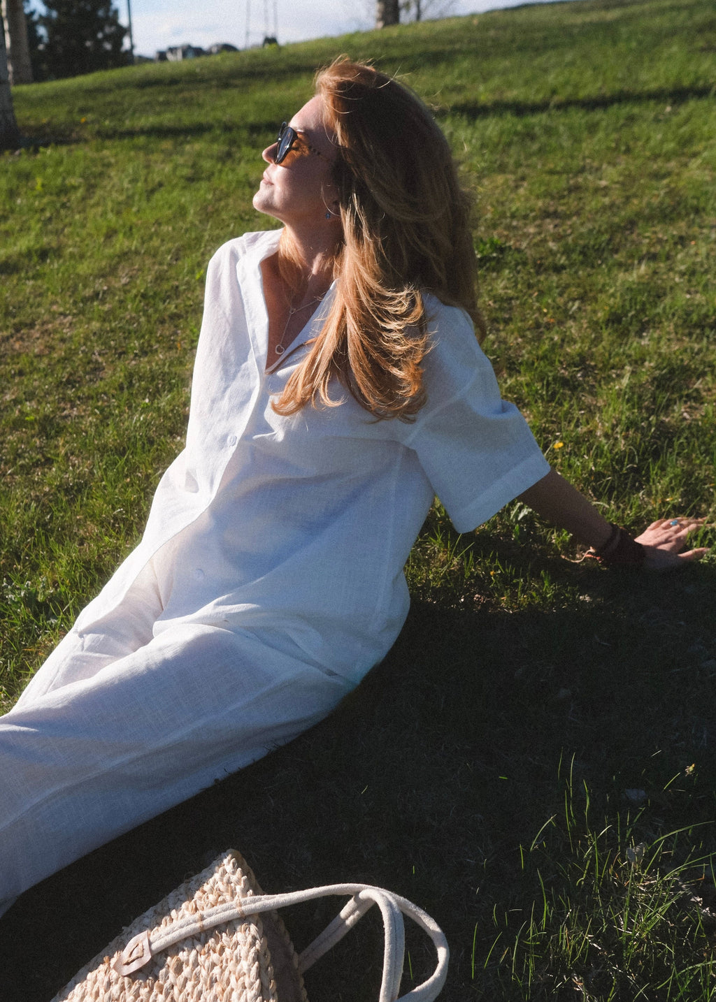 Woman in a white dress sitting on grass wearing sunglasses