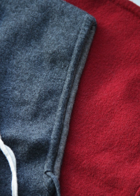 Close-up of folded fabric in two colors: a dark heather gray on the left and a deep red on the right, with a small white cord detail visible at the lower left.