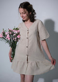 Woman wearing a beige dress holding pink flowers against a plain background