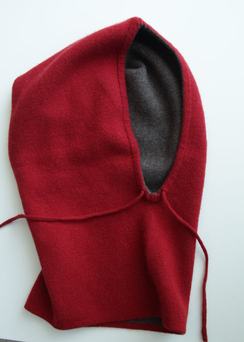 A red wool balaclava hood with a dark gray inner lining, laid flat on a white surface.