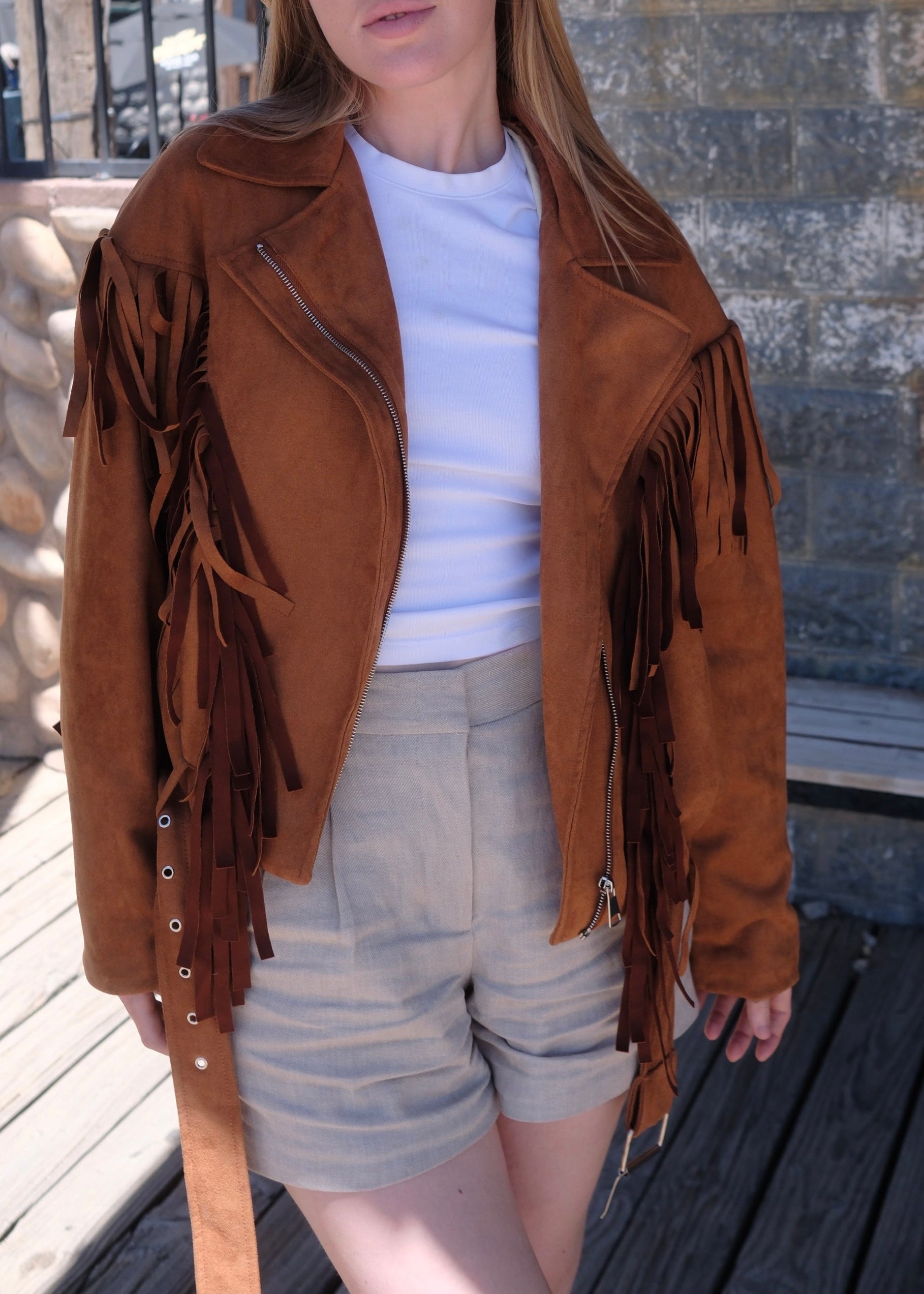 Person wearing a brown fringed jacket outdoors on a wooden deck.