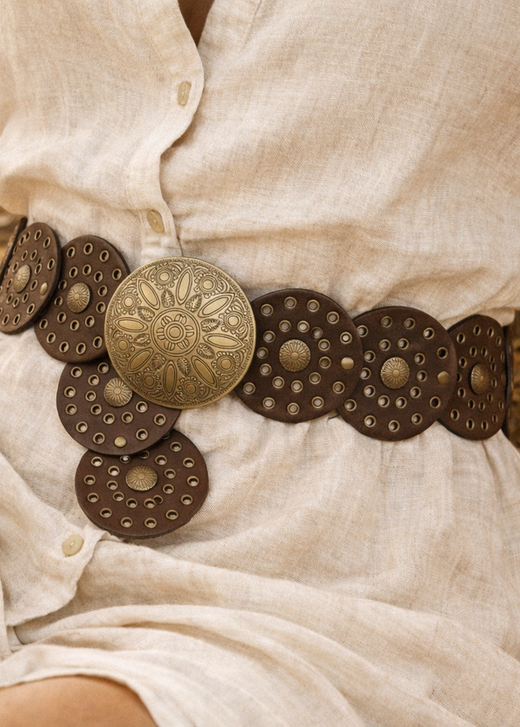 Person wearing a white shirt with a decorative  western brown belt featuring large circular medallions.