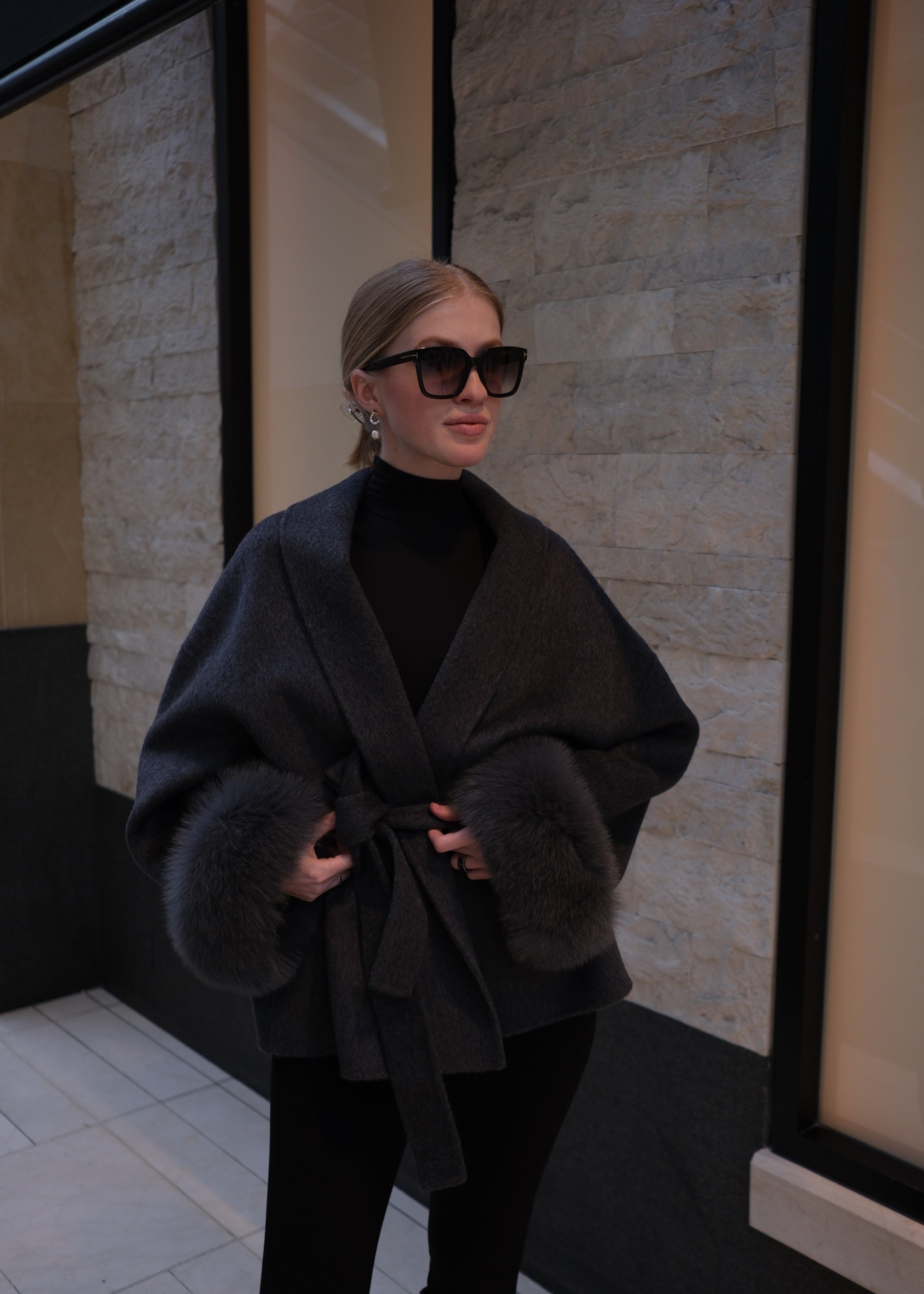 Person wearing a dark coat with fur trim in an indoor setting