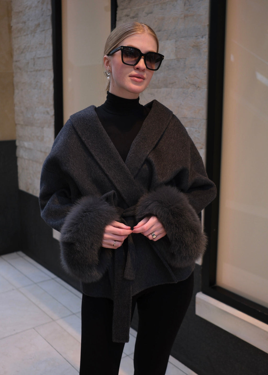 Woman wearing a charcoal grey luxury wool wrap coat with genuine rabbit fur cuffs, belted waist, oversized collar and elegant winter style.